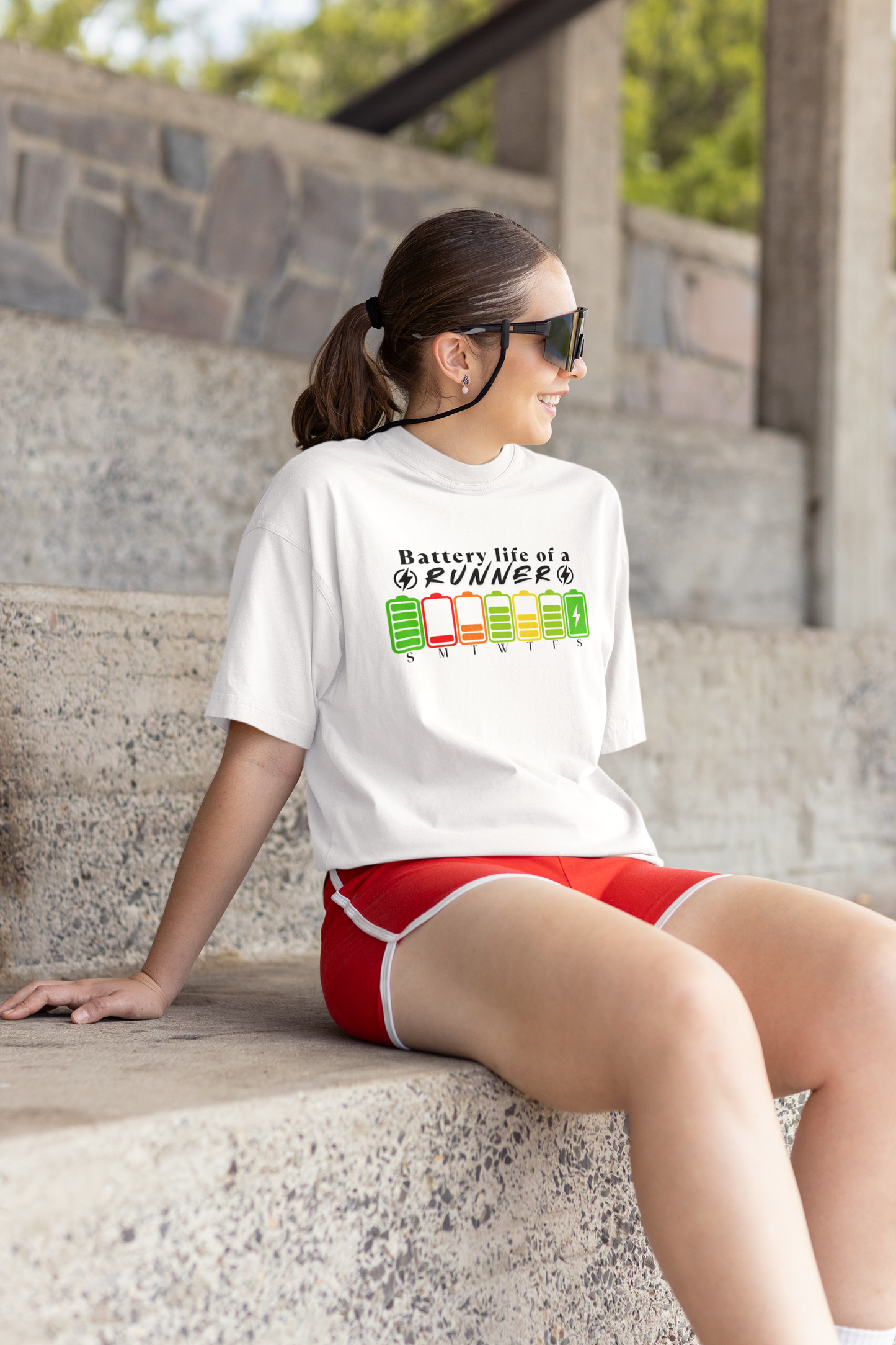 Woman sitting wearing "Battery Life of a Runner" shirt – motivational running tee with weekday battery icons