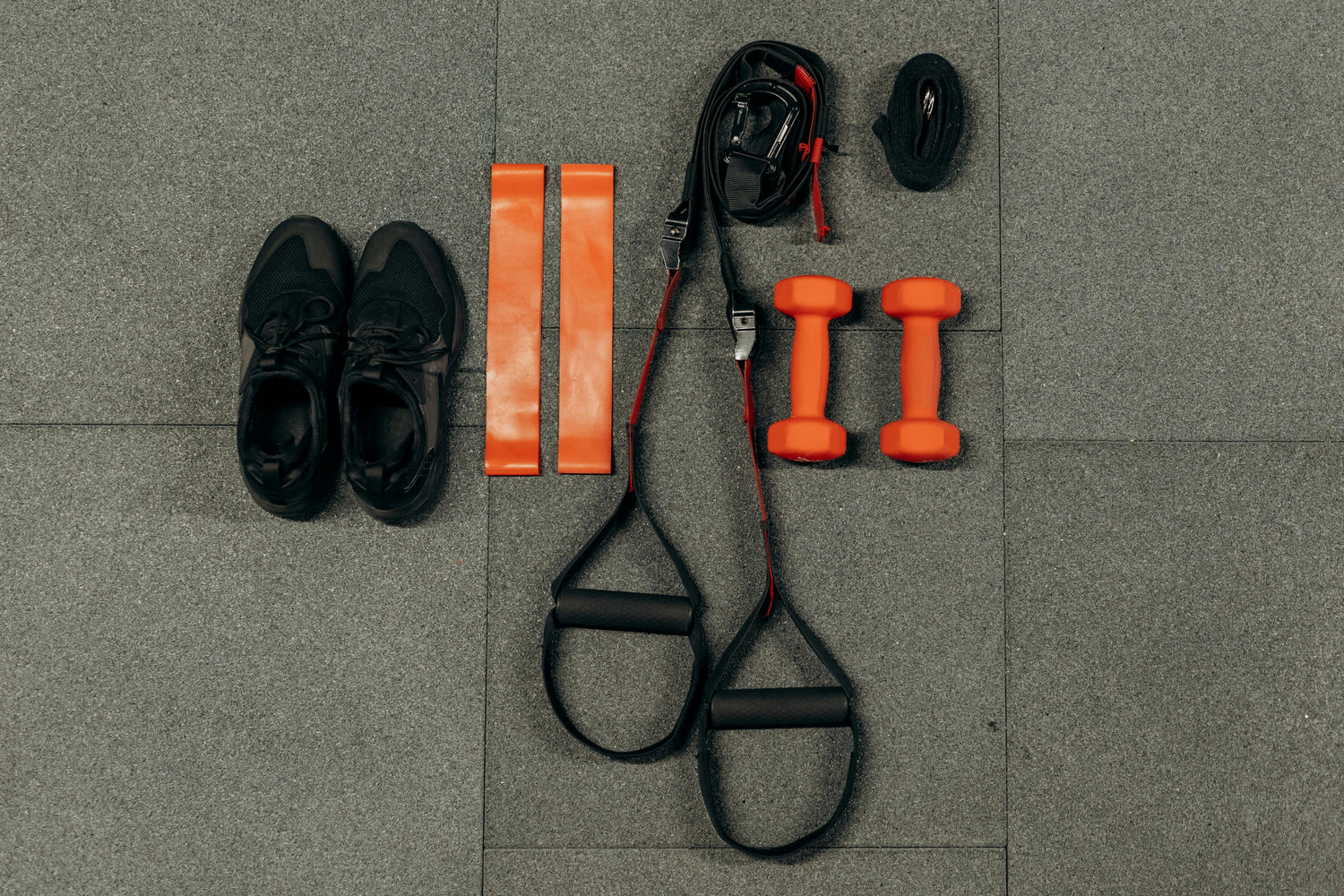 Flat lay of home gym accessories including dumbbells, resistance bands, gym gloves, and shoes – FitBOUND gear for runners and lifters