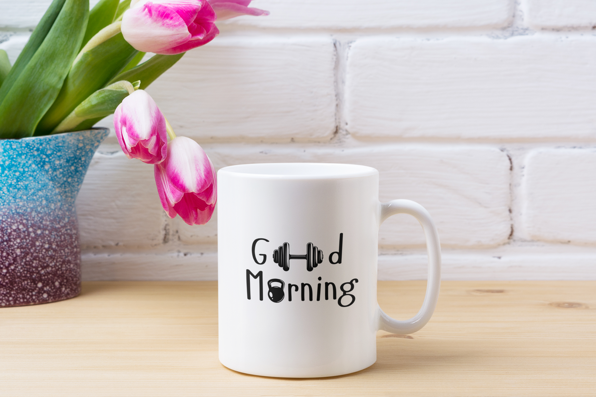 “Good Morning” ceramic mug on a wooden table with pink flowers and a book – calm and relaxing morning setup by FitBOUND