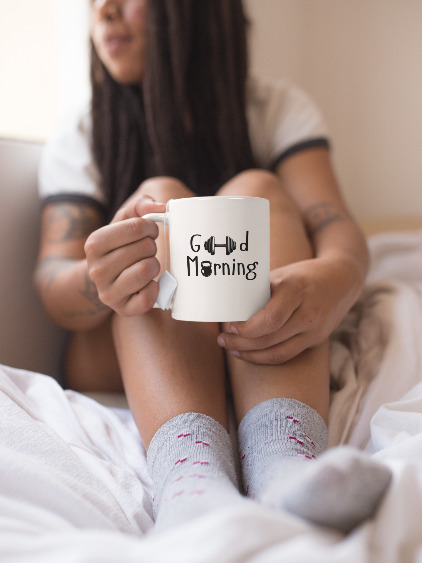 Woman sitting on a sofa holding “Good Morning” coffee mug – warm and cozy lifestyle scene with FitBOUND ceramic cup