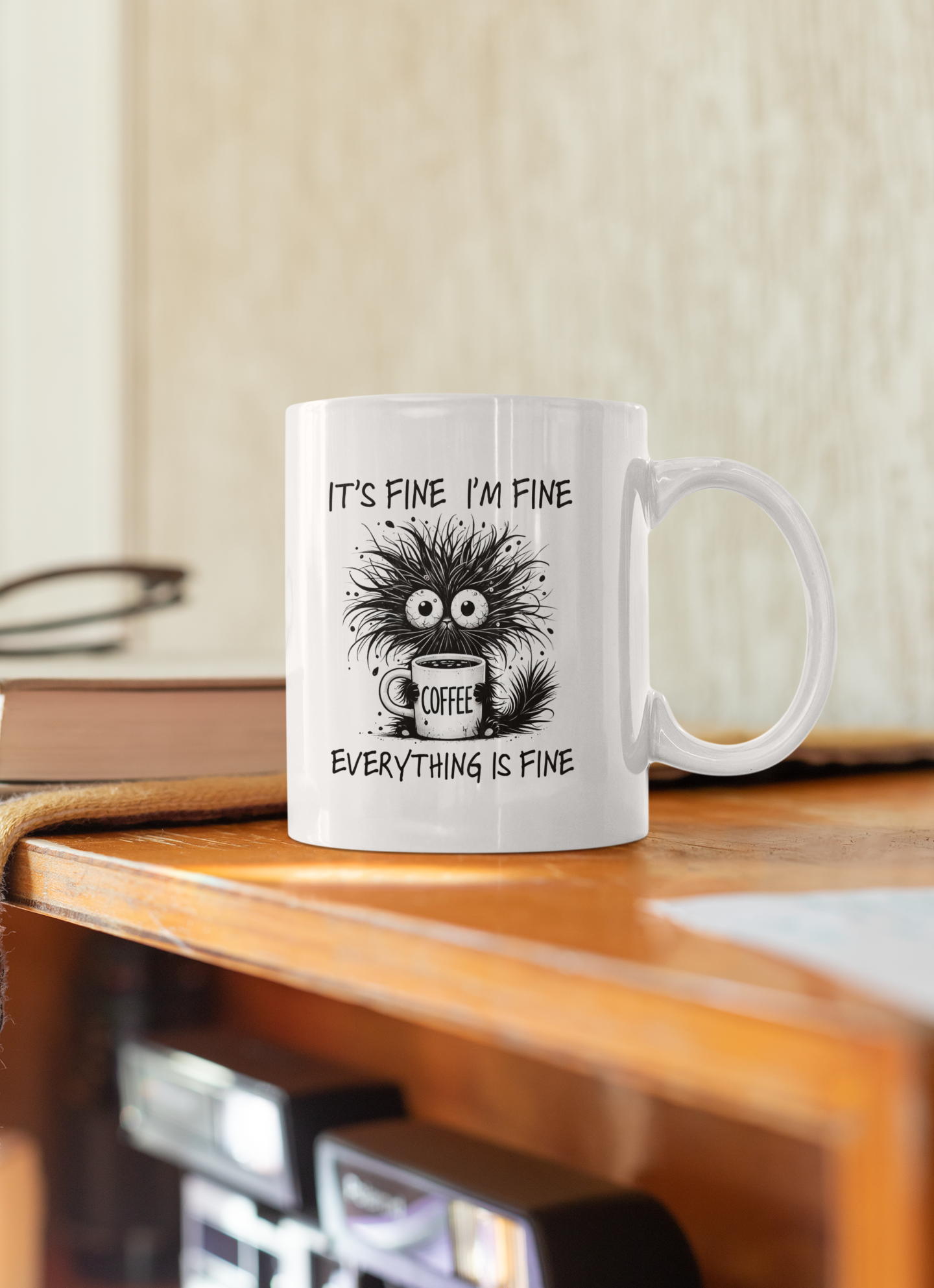 White ceramic coffee mug on wooden desk with humorous design “It’s Fine I’m Fine Everything Is Fine” – stress relief cup.