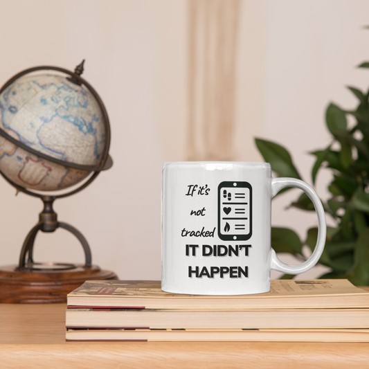 White ceramic mug with the phrase “If it’s not tracked it didn’t happen” displayed on books with globe and plant decor