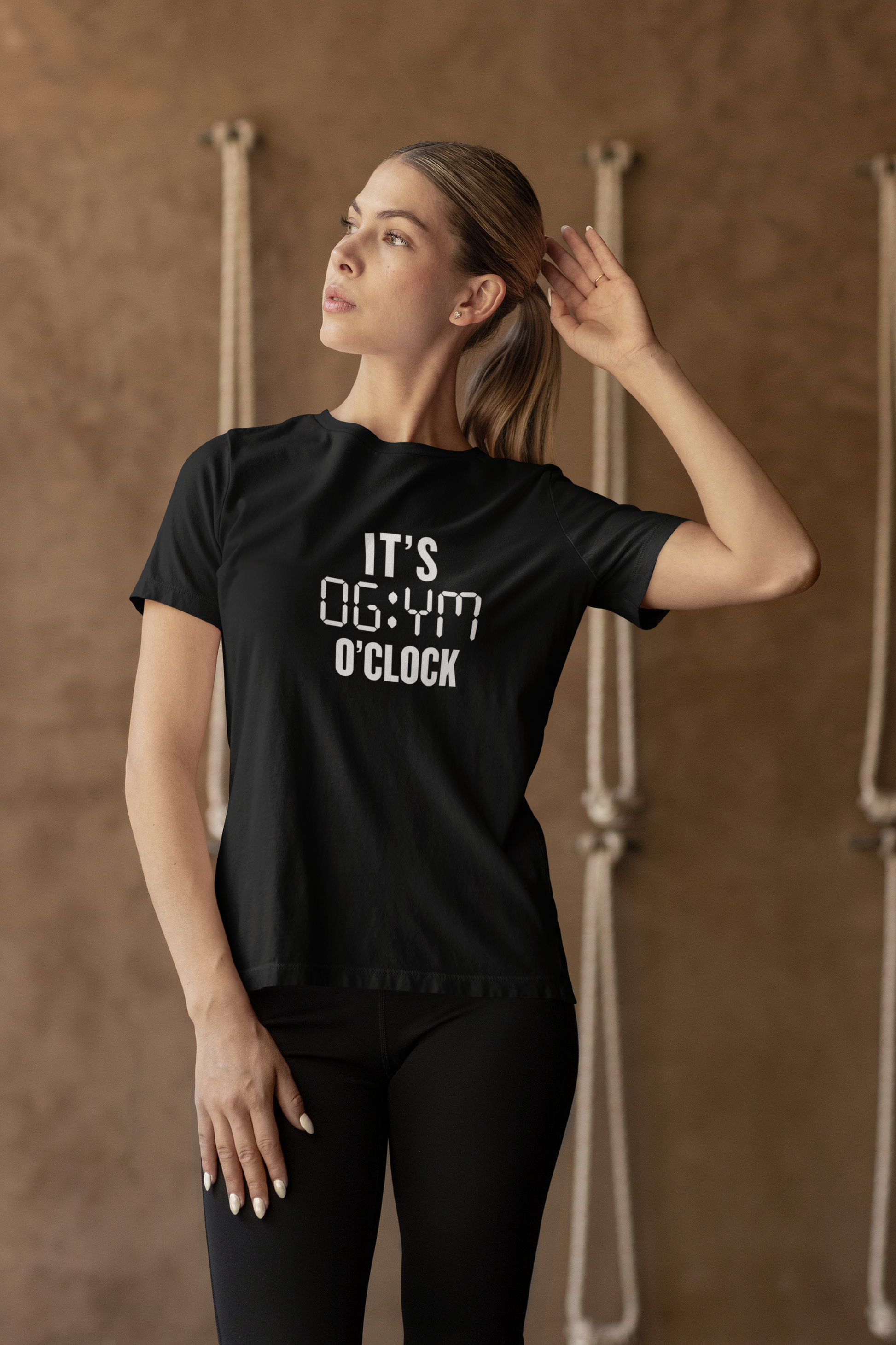 Woman stretching in a fitness studio while wearing black “It’s Gym O’Clock” T-shirt – motivational activewear by FitBOUND